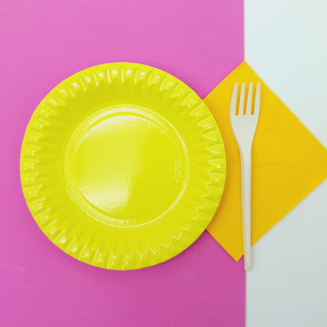 Apparecchiatura con piatto di carta giallo, tovagliolo di carta giallo, forchetta di plastica su tovaglietta rosa